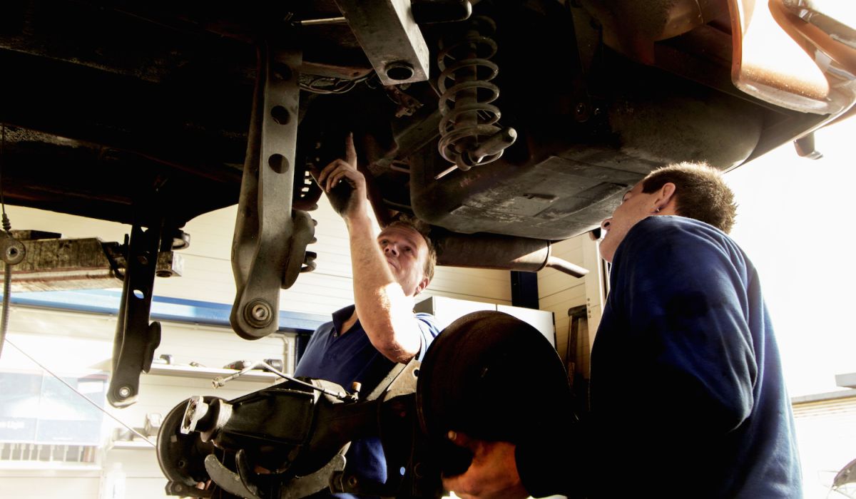 två studeranden håller på med en reparation av ett hjulhus på en personbil