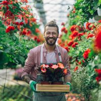 En man håller i korg av blommar i ett växthus som driver blommor