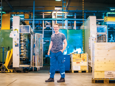 Ung manlig person står i en maskinhall med lager och maskiner i bakgrunden